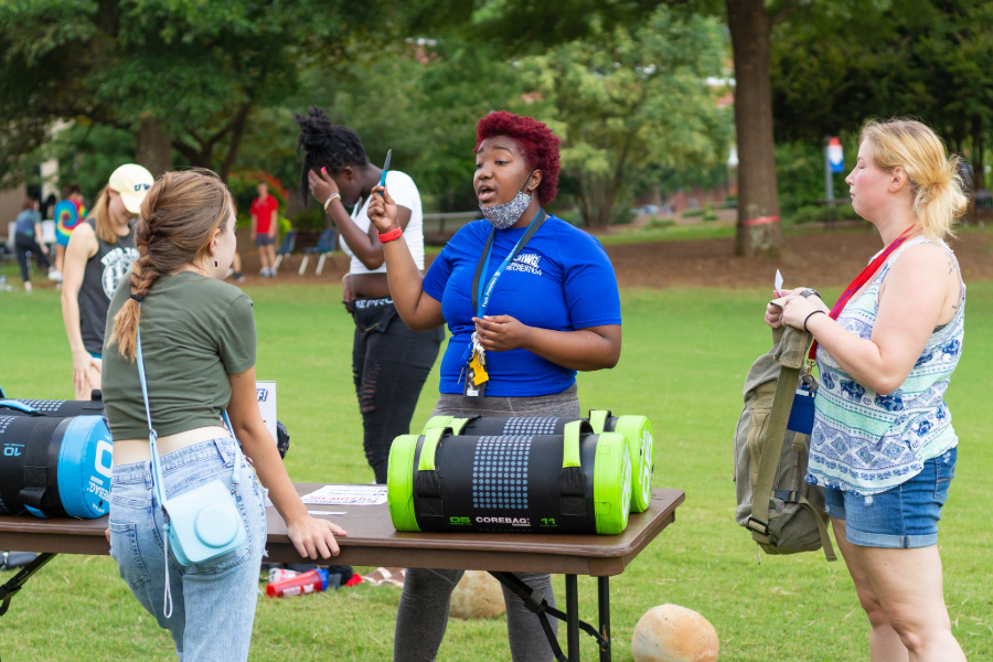 Students speaking with uwg employee at an outdoor table.