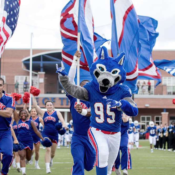 Wolfie and the UWG Cheer team running onto the football field
