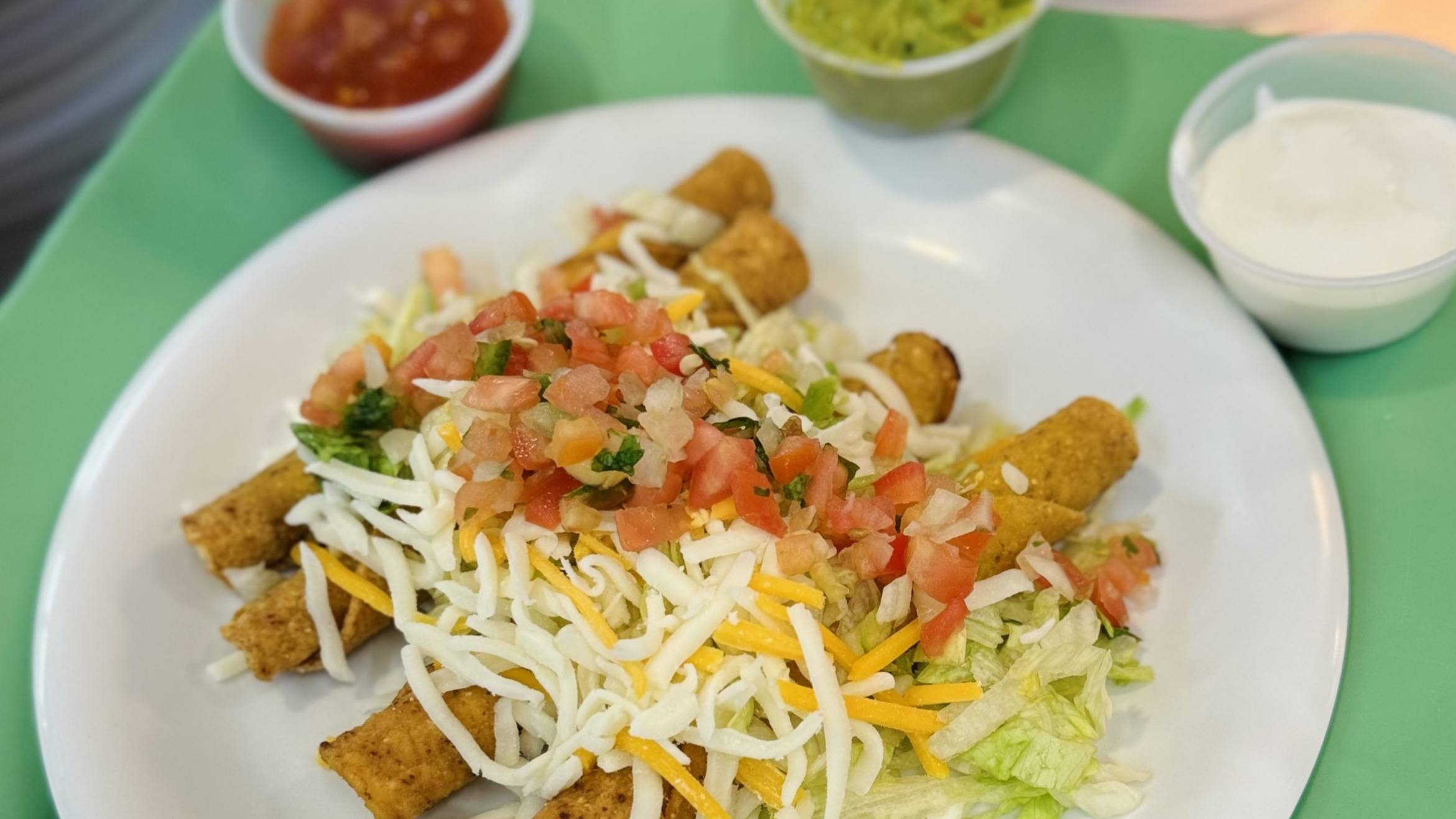 Taquitos with lettuce, cheese, and pico de gaio on top.