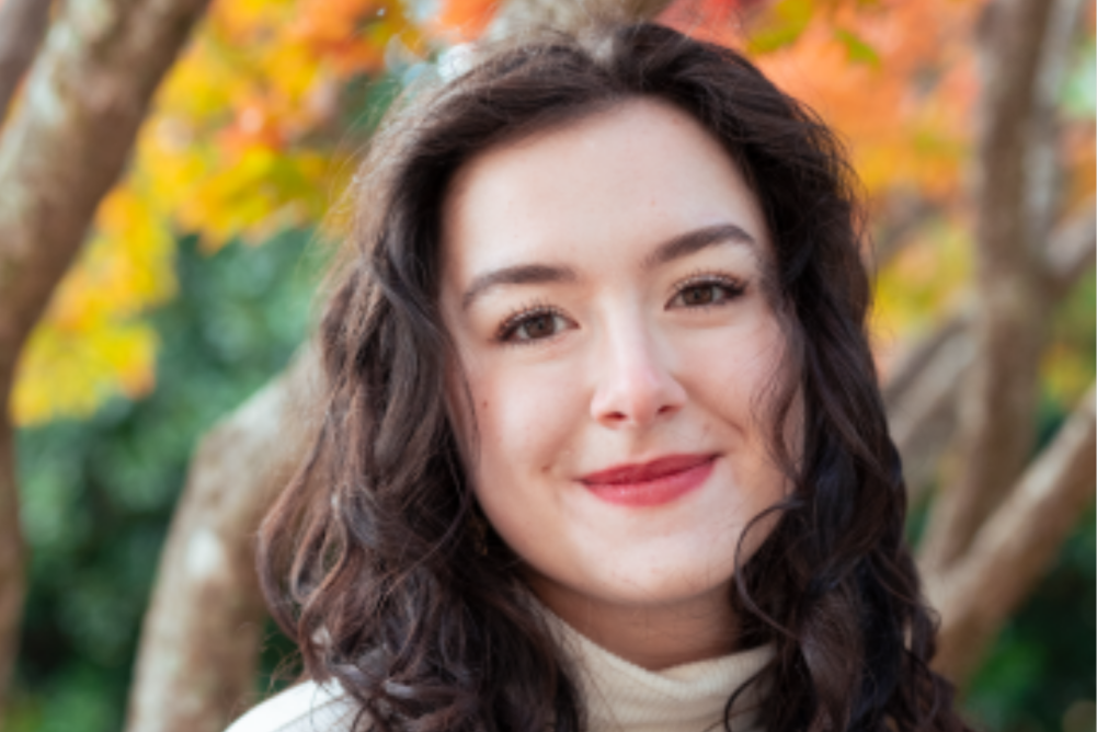 brown haired women smiling at camera with fall trees in background