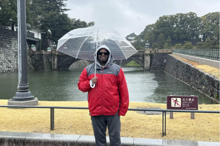 man standing in the rain in a red raincoat holding a clear umbrella.