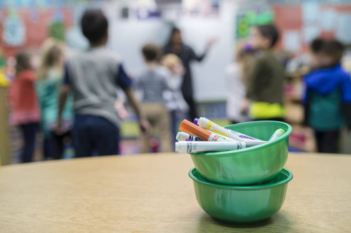 Teacher working with a group of students behind a bowl of markers on a table.