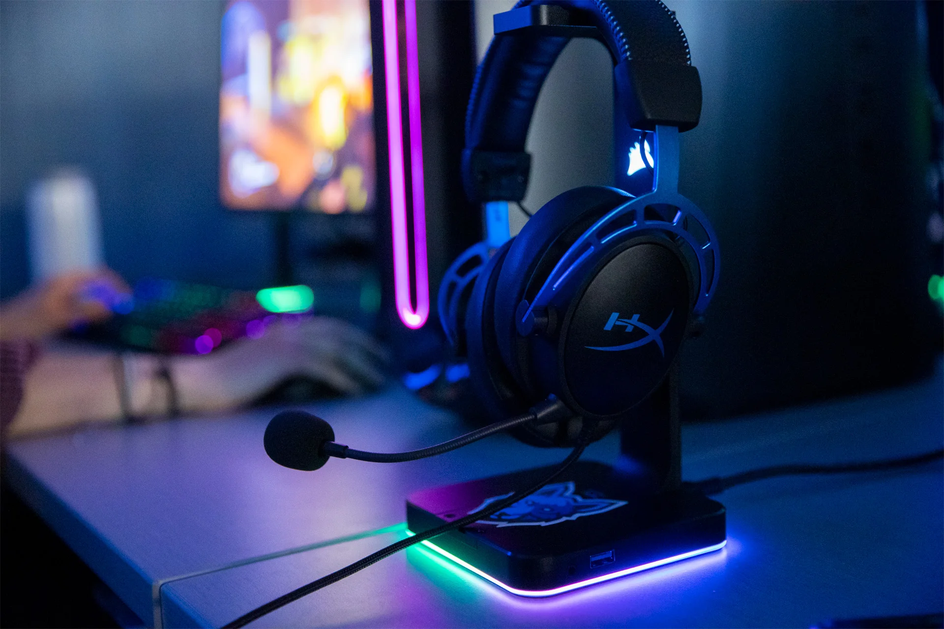 Close up of gaming headset with microphone sitting on a stand beside a PC.