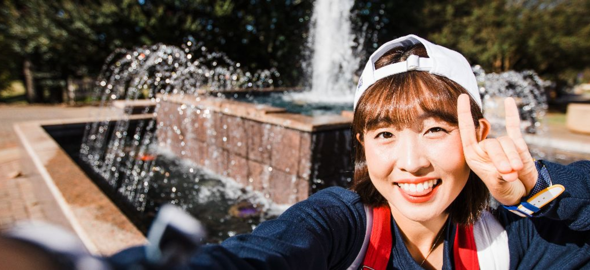 girl giving wolf hand gesture in front of fountain