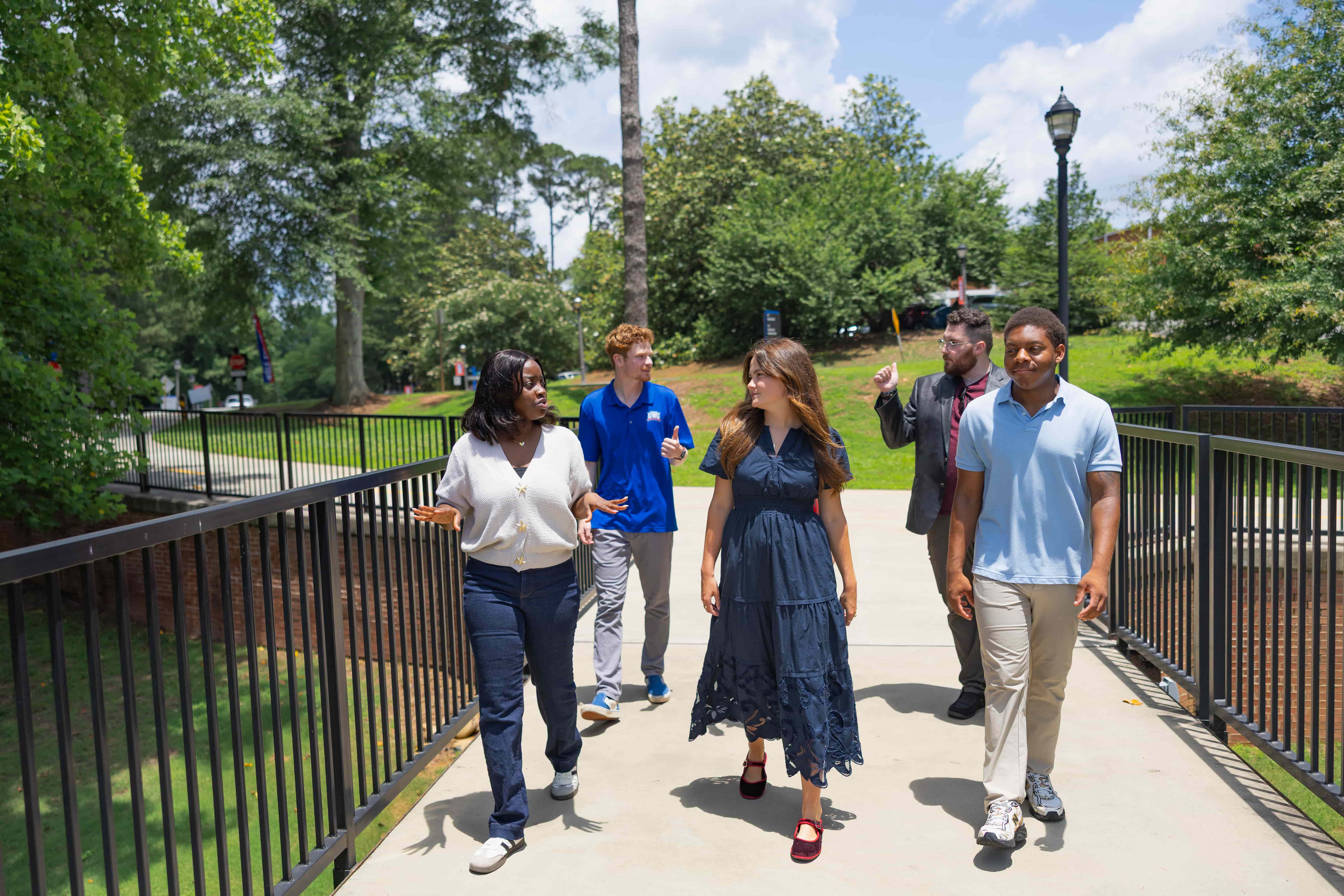 A group of students walking across a bridge outside on a sunny day
