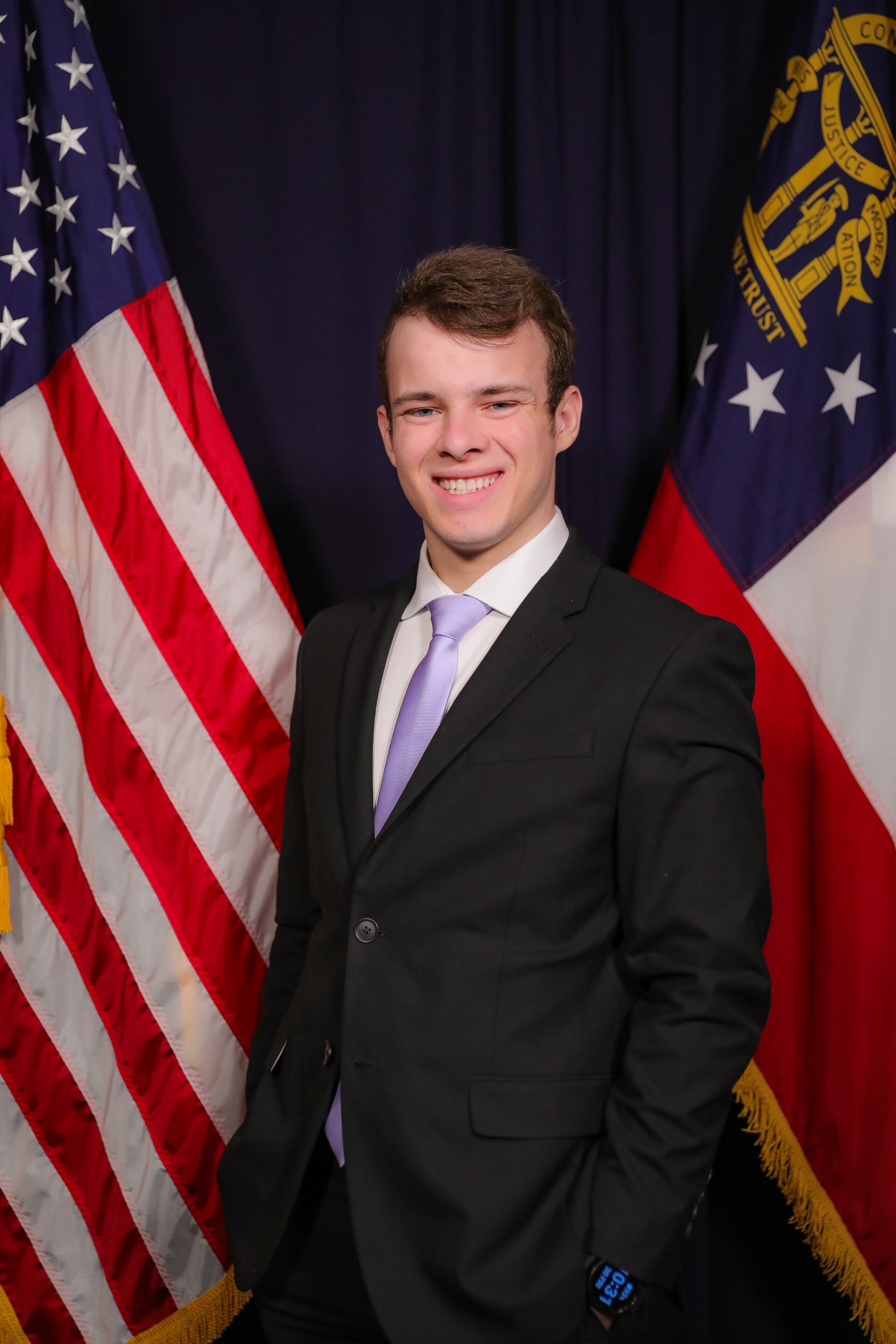 Student in a suit standing in front of Georgia and American flags.