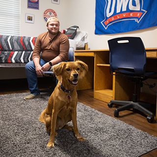 Student sitting in a chair in their bedroom with a dog in front of them. 