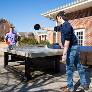 Two students playing ping-pong outside. 
