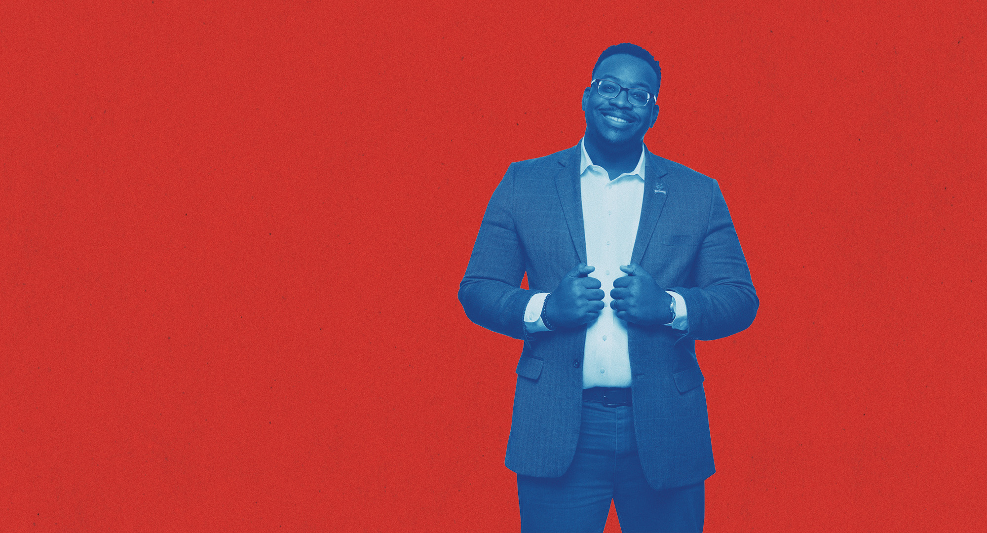 UWG Student dressed in a suit posing and smiling in front of a red background.