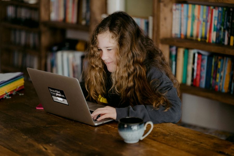 Female student sitting in the library looking at her computer screen and smiling.