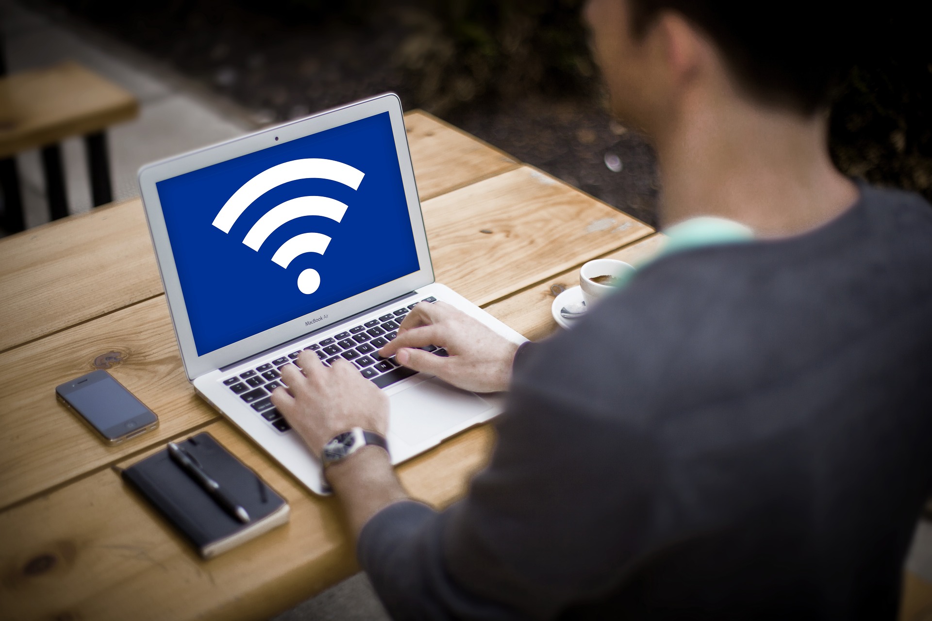 Man on laptop with screen showing large "wifi" symbol.