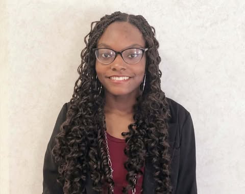 Woman in with curly hair in glasses standing against a blank background