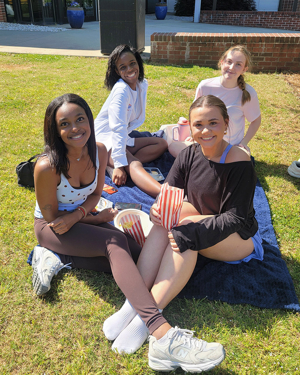 Four students sitting on the grass eating popcorn at Newnan Campus