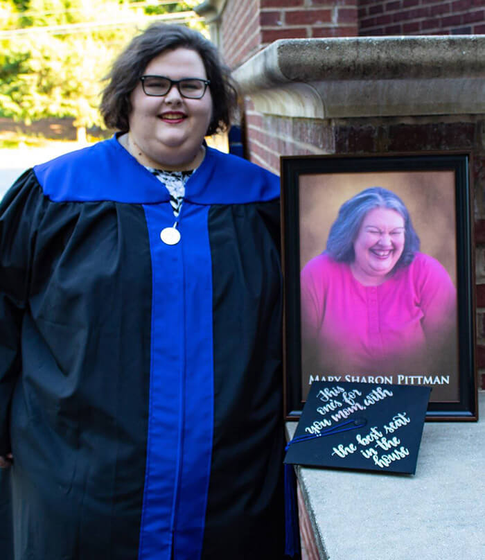 Molly Pittman in graduation regalia holding a photo of her mother
