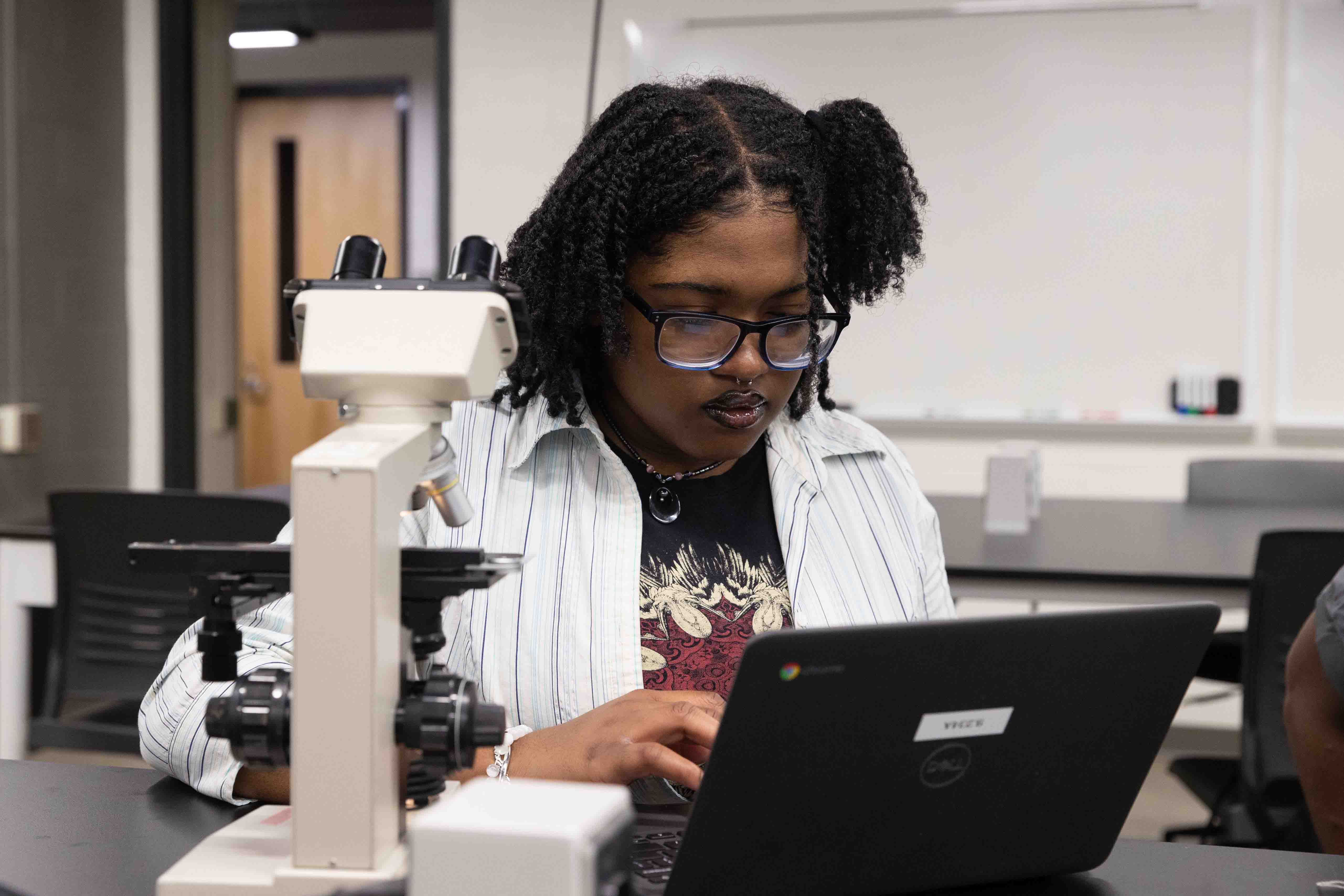 A female student conducting an experiment in a scientific lab with a laptop in front of her.