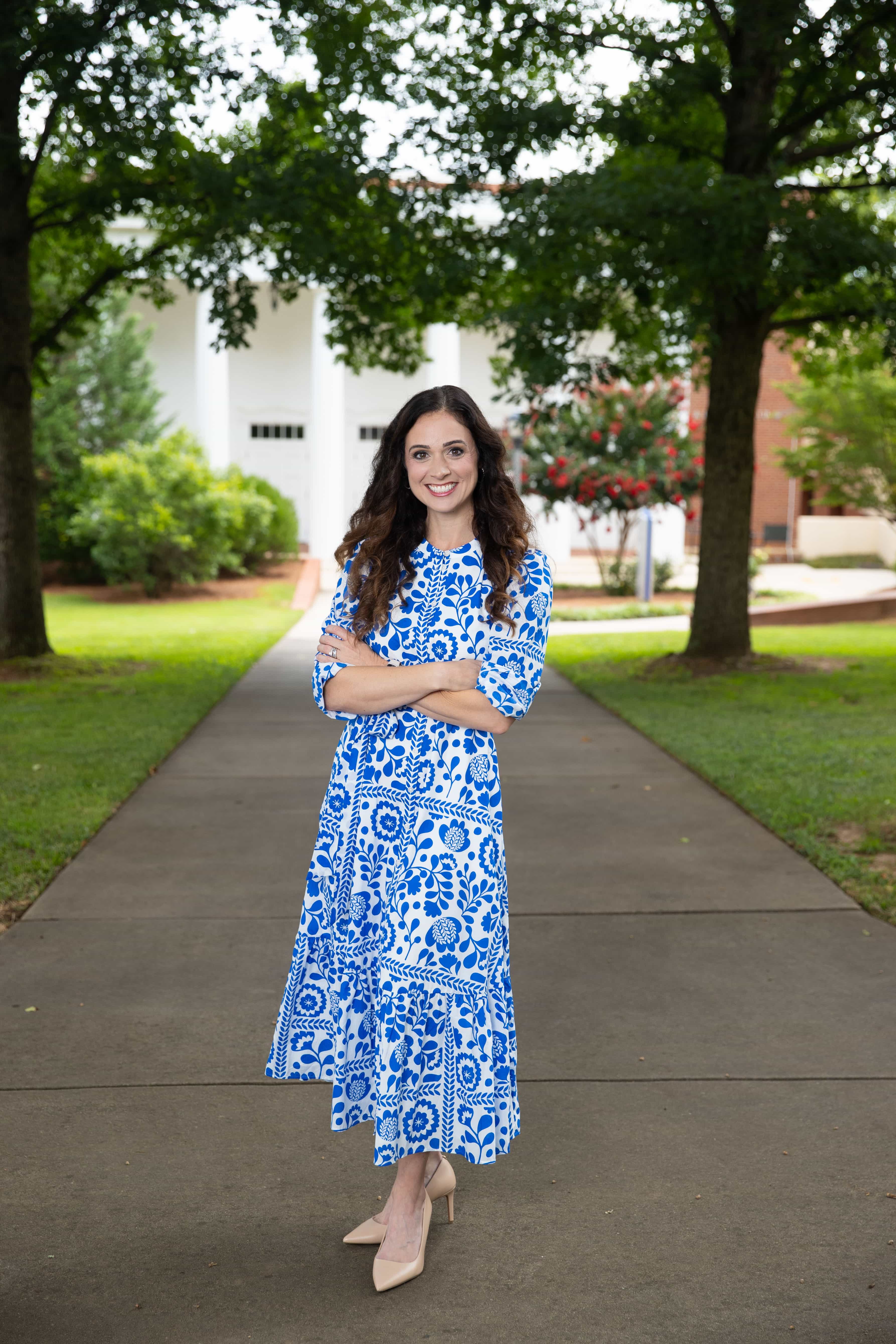 First Lady, Beth Johnson, wearing a blue and white dress smiling for an outdoor photo on campus.