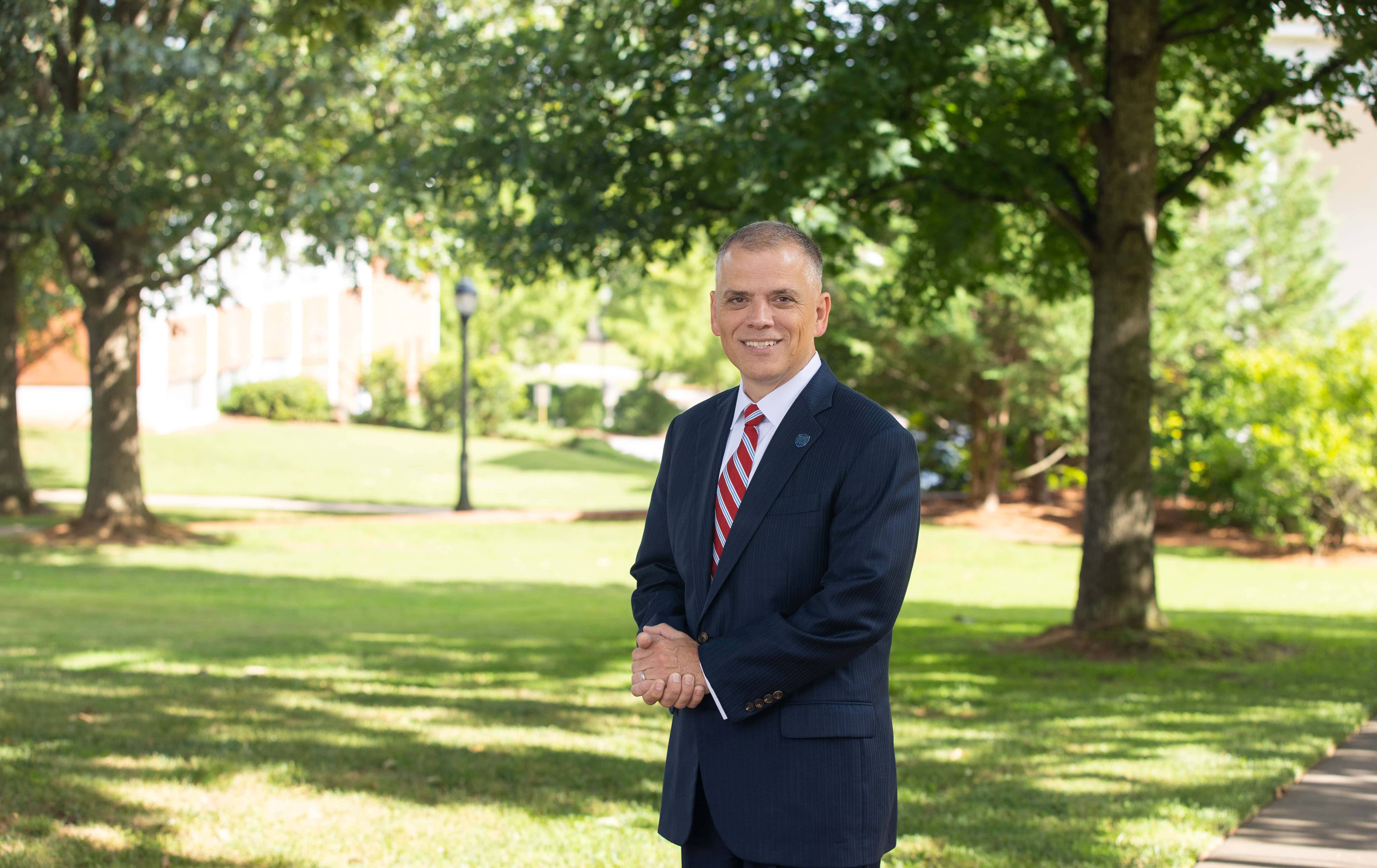 President Johnson standing outside for a professional photo, wearing a suit with a red and white striped tie.