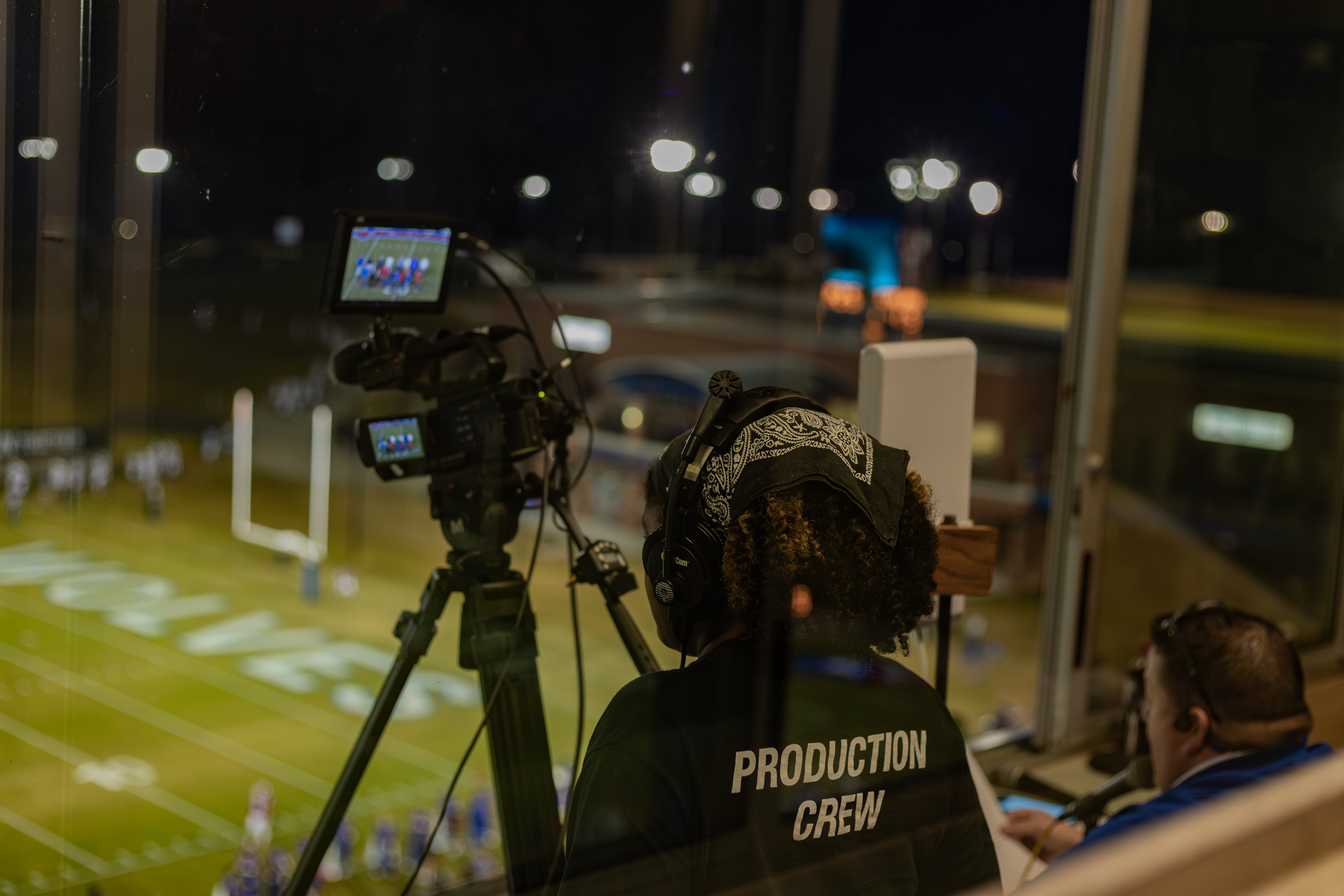 Production student standing in press box at the university stadium, filming a football game.
