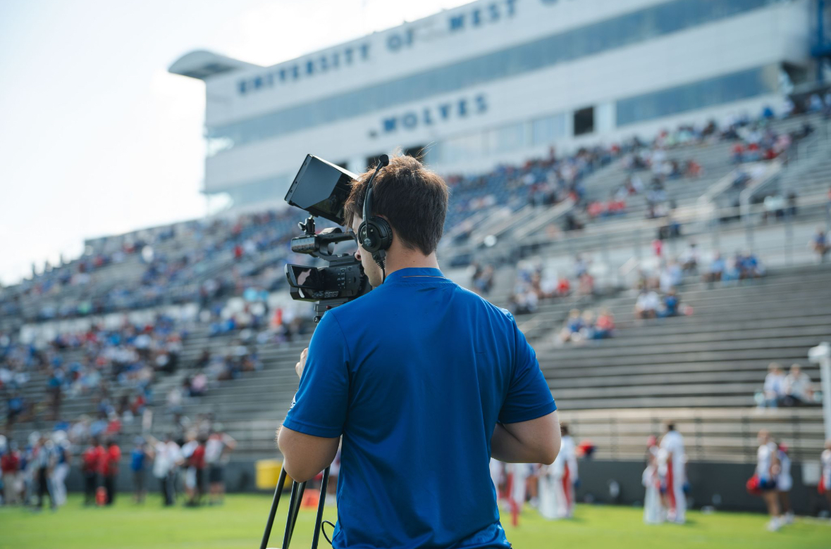 Productions student filming on football field during game.