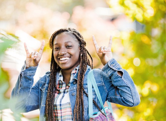 Student smiling outside holding up the wolf sign.