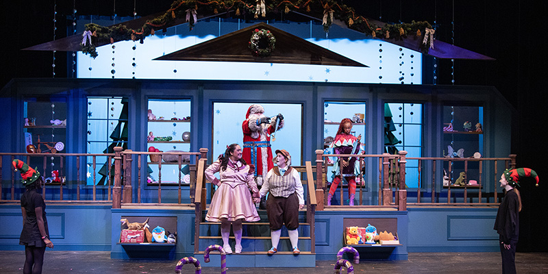 Costumed actors on holiday-themed stage set resembling a toy shop.