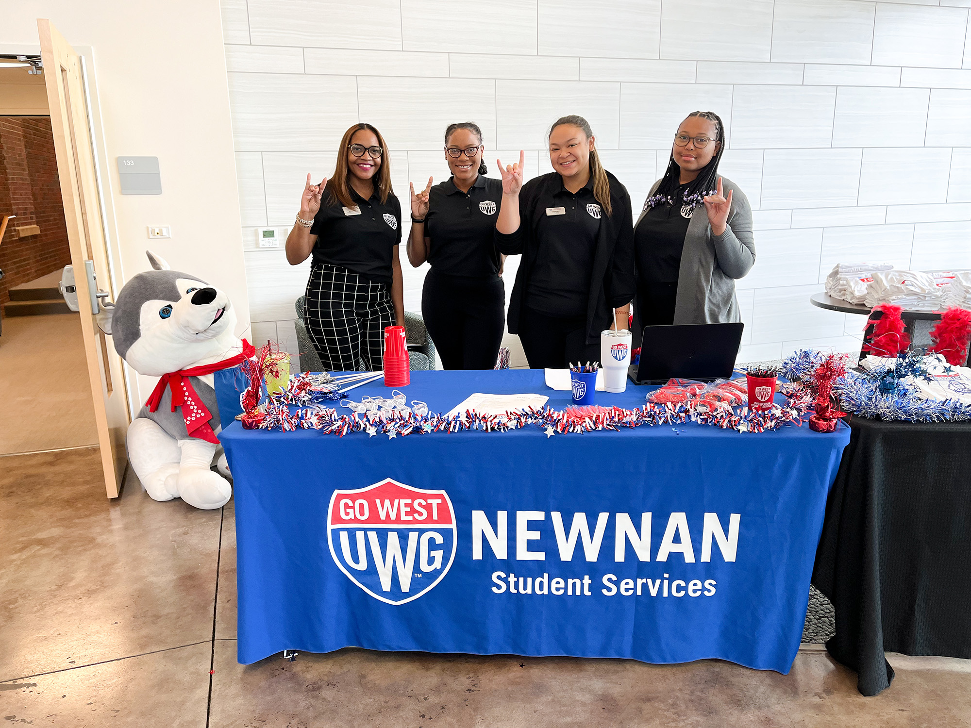 Newnan workers tabling for Newnan Student Services holding the wolf hand sign