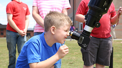 A child squints through the eyepice of a refractor telescope