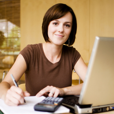 Female looking at the camera, sitting at her desk holding a pen with her computer in front of her.